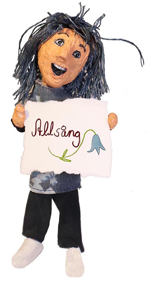 En dockfigur med blått hår och glatt leende håller upp en skylt där det står Allsång.